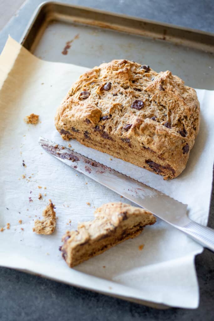 a stout chocolate chip soda bread loaf on a parchment-lined baking sheet with a serrated knife