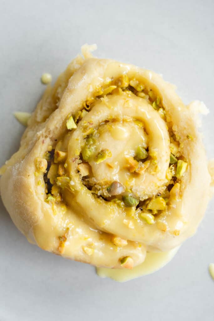 a vegan lemon pistachio sweet roll on a plate topped with a lemon glaze