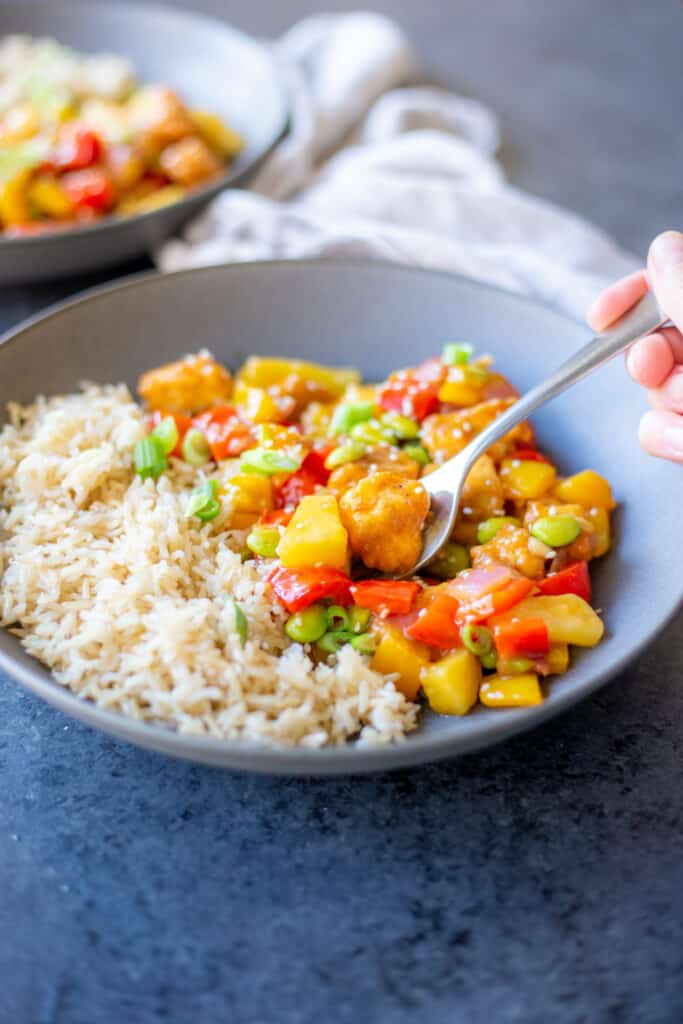 a fork dipping into a bowl of pineapple, veggie, and tofu stir fry
