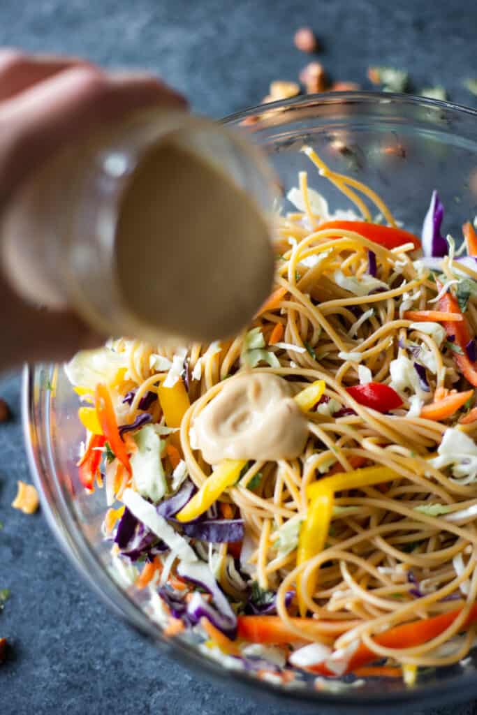 a hand pouring Garlicky Gingery Almondy Protein Sauce onto noodles and vegetables