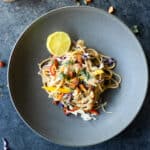 a bowl of colorful vegetable noodles with a garlic, ginger, almond, protein sauce on top