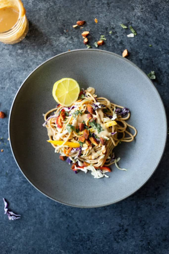 a bowl of colorful vegetable noodles with a garlic, ginger, almond, protein sauce on top