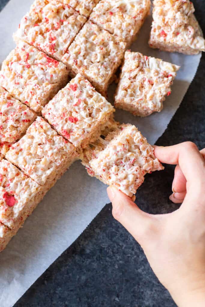 a hand pulling a strawberries and cream crispy rice treat from the pile