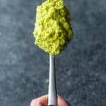 a spoon full of vegan garlic scape pesto held by a hand