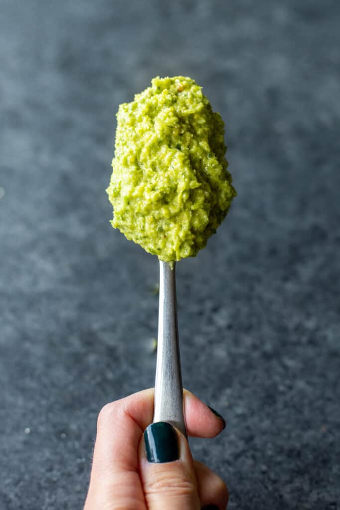 a spoon full of vegan garlic scape pesto held by a hand