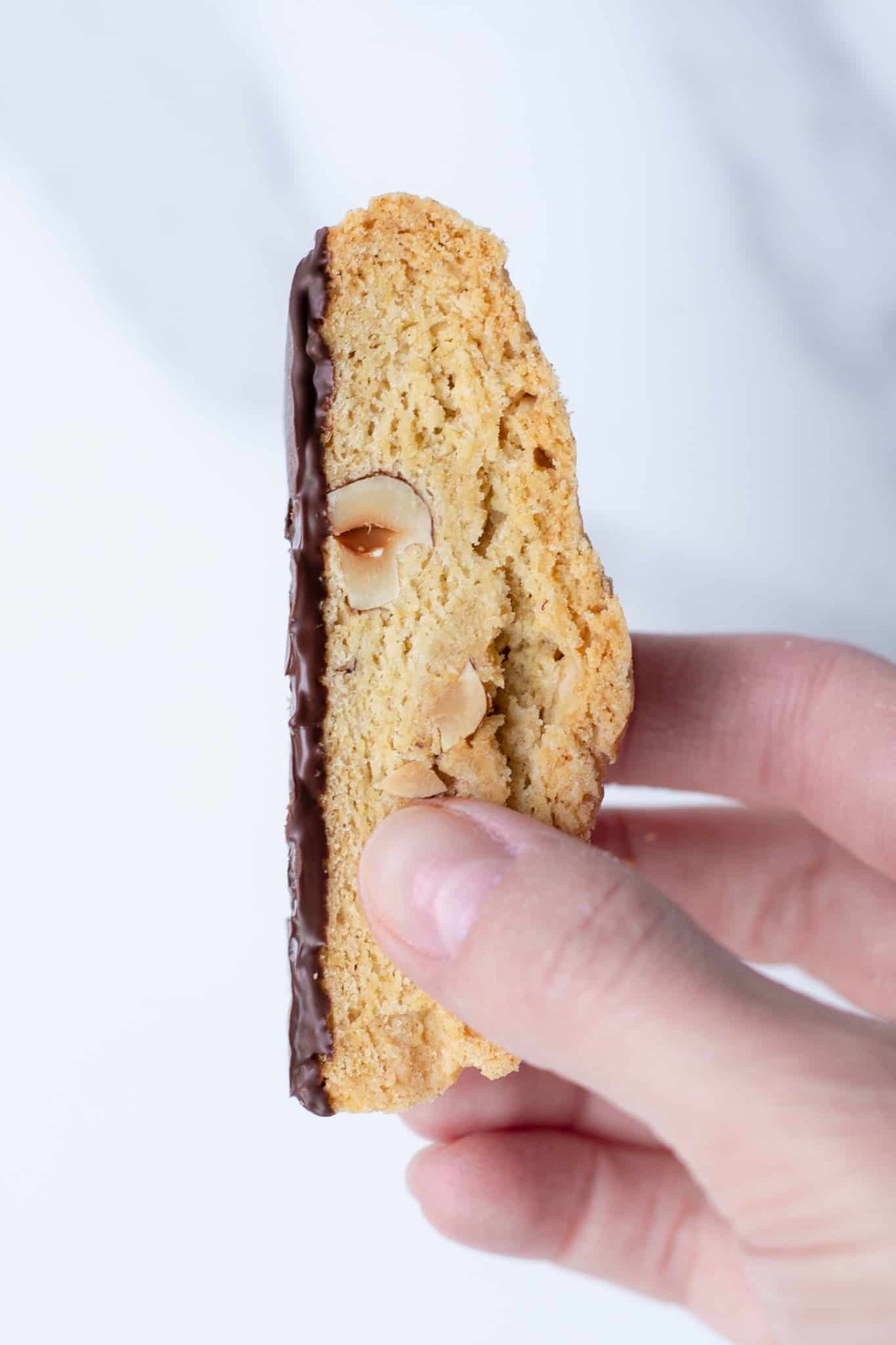 a hand holding a vegan chocolate hazelnut biscotti against a marble background
