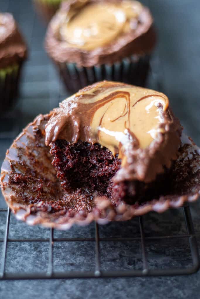 a bite taken out of a vegan chocolate cupcake with chocolate peanut butter ganache frosting