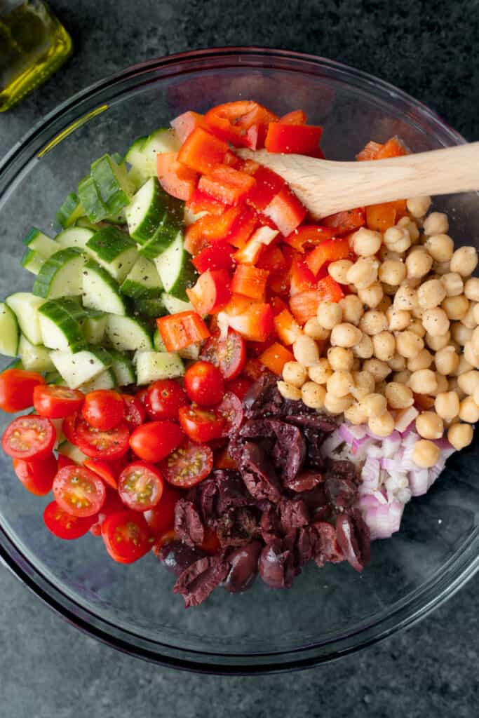 Diced cucumbers, bell pepper, chickpeas, shallot, kalamata olives, and grape tomatoes in a glass bowl