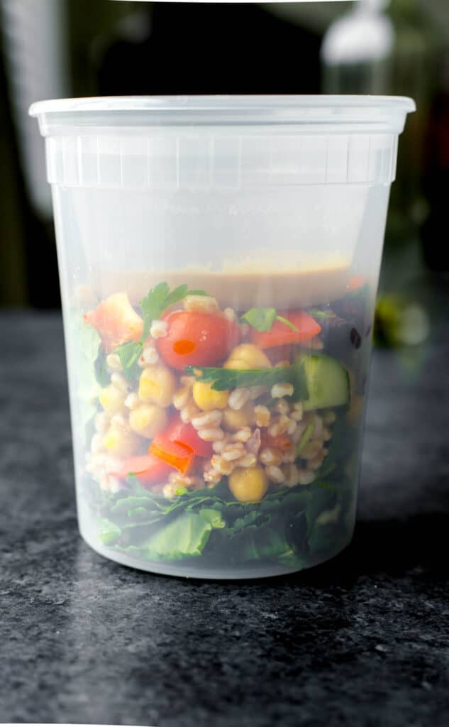 farro grain bowl in a meal prep container with the dressing on top