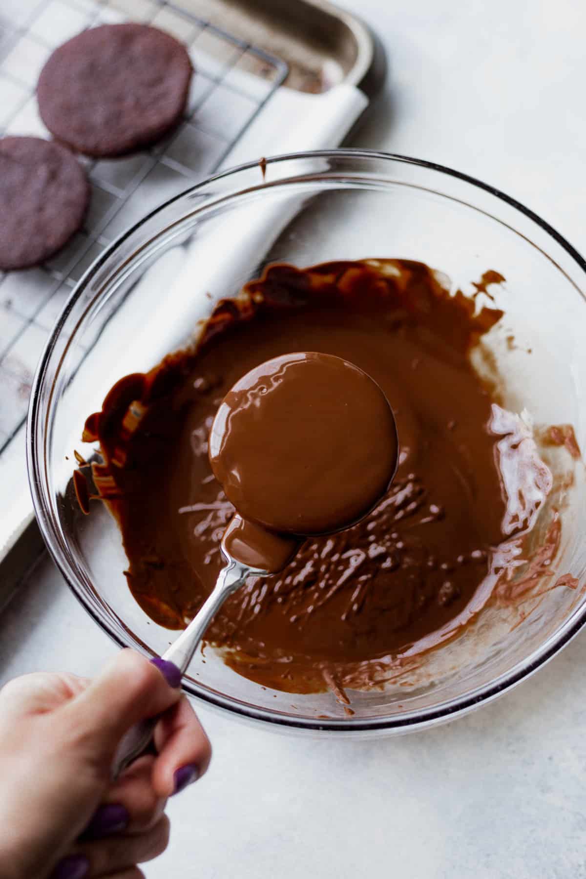 a hand dipping a vegan thin mint in melted chocolate