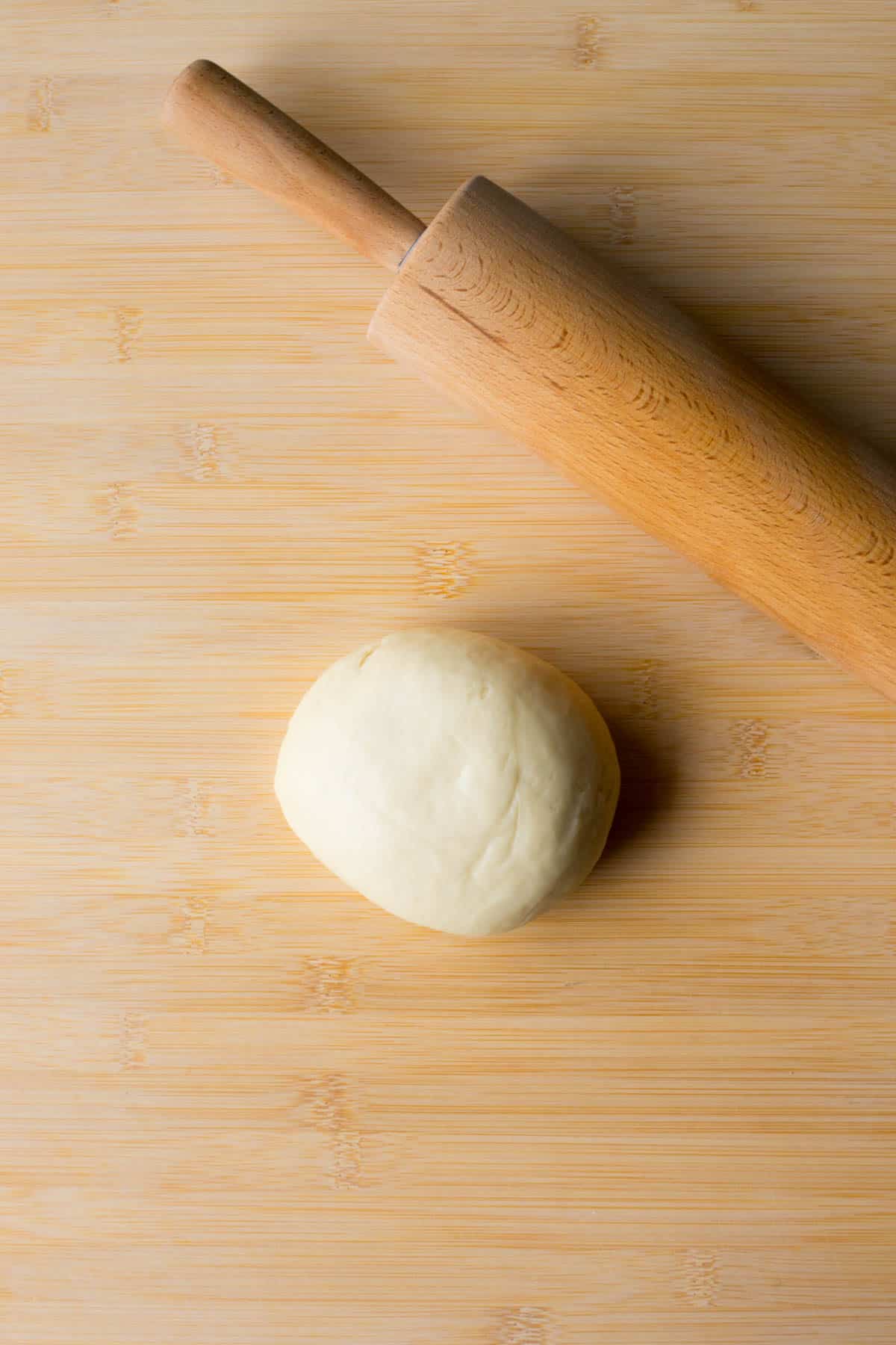 a ball of vegan pasta dough on a cutting board with a rolling pin