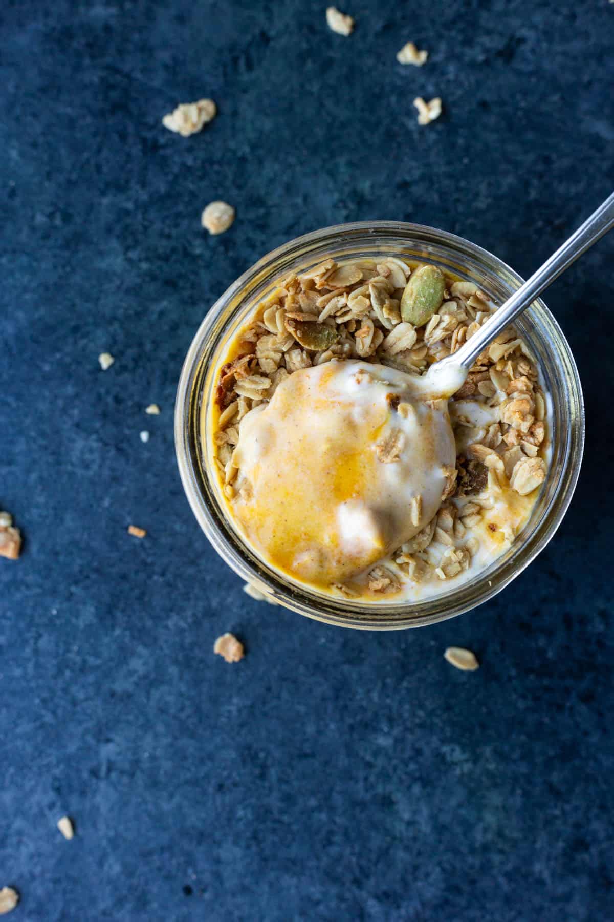 a spoon dipped into a vegan pumpkin swirl yogurt parfait topped with granola