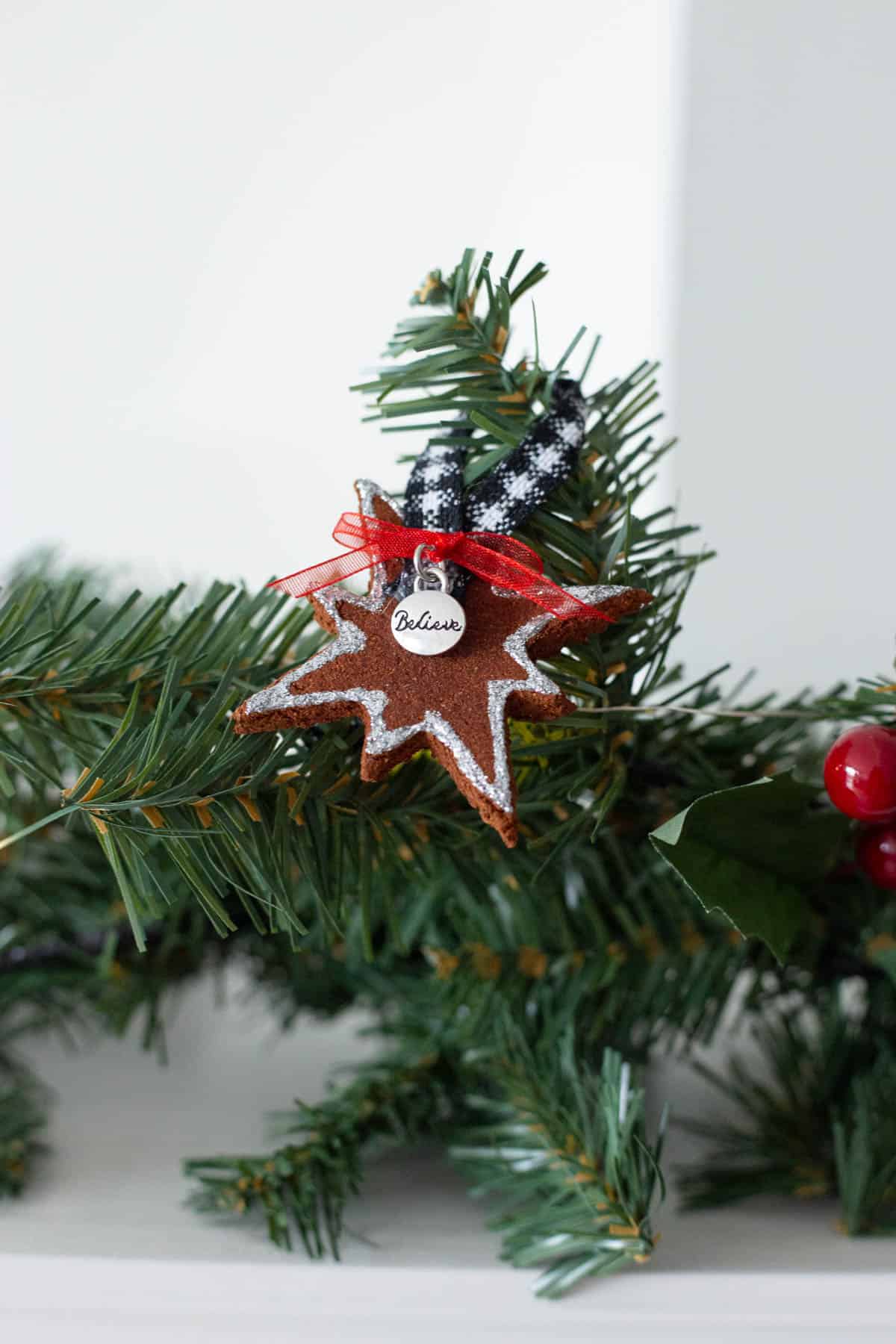 a star cinnamon ornament with a charm that says 'Believe' hanging on a garland