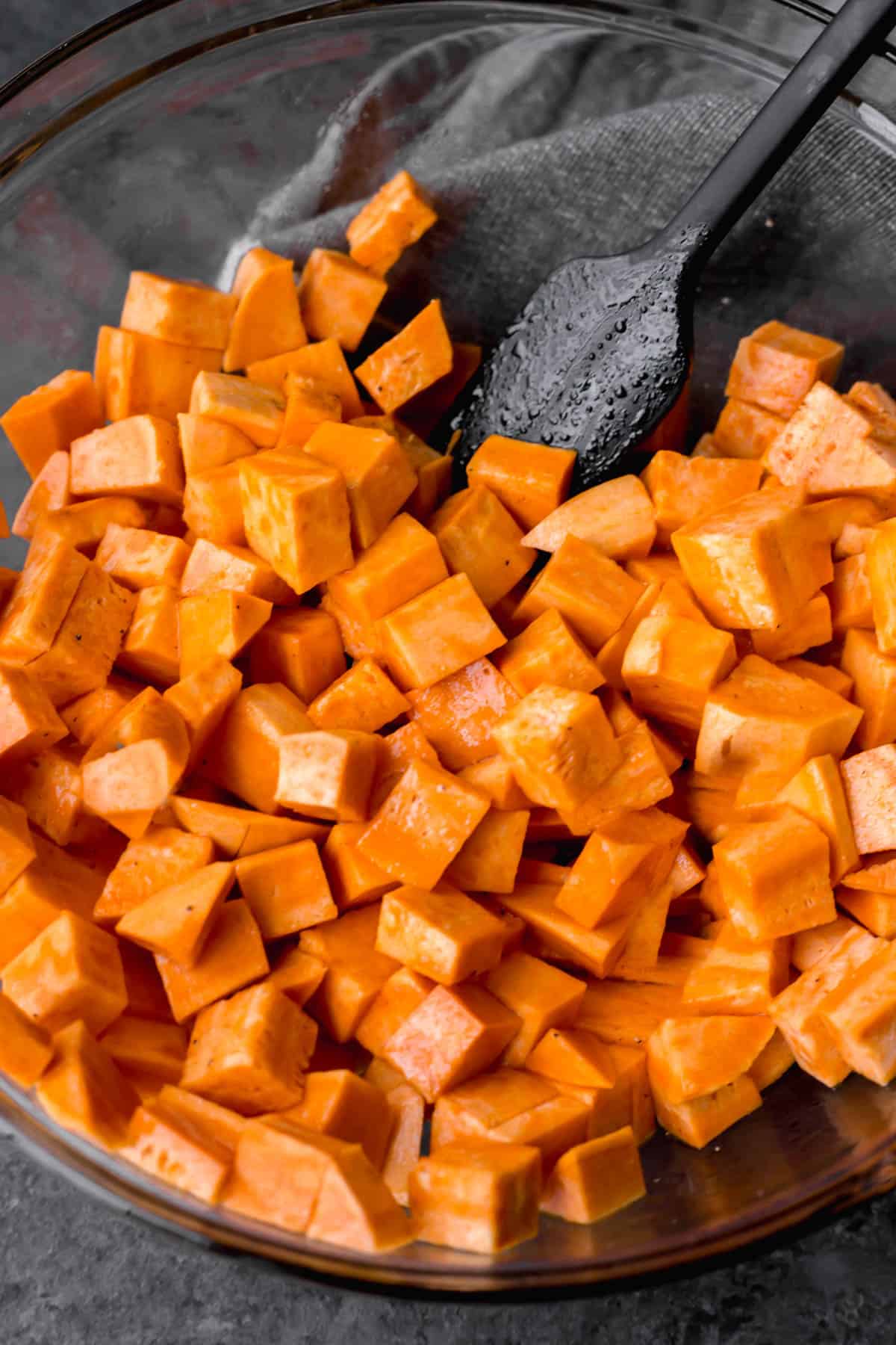 a bowl of raw sweet potatoes in a bowl with a black spatula