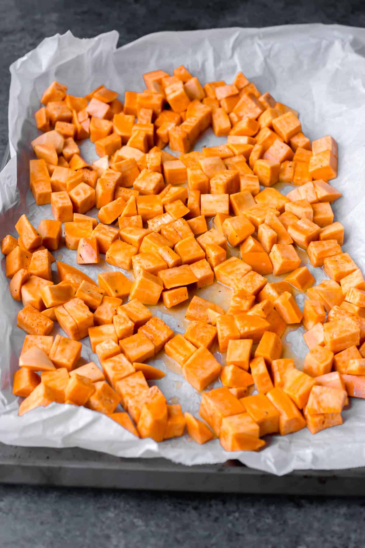 a parchment-lined baking sheet with cut sweet potatoes on top