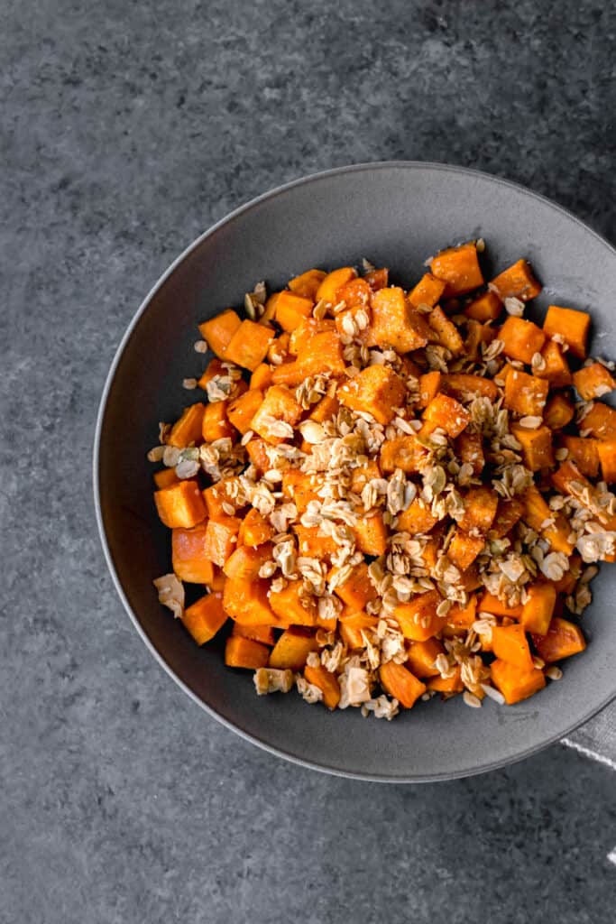 a bowl of granola-topped vegan maple roasted sweet potatoes