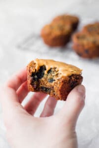 a hand holding a vegan blueberry walnut oatmeal muffin topped with peanut butter