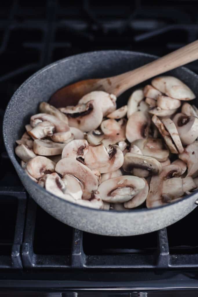 raw mushrooms in a pan with a wooden spoon